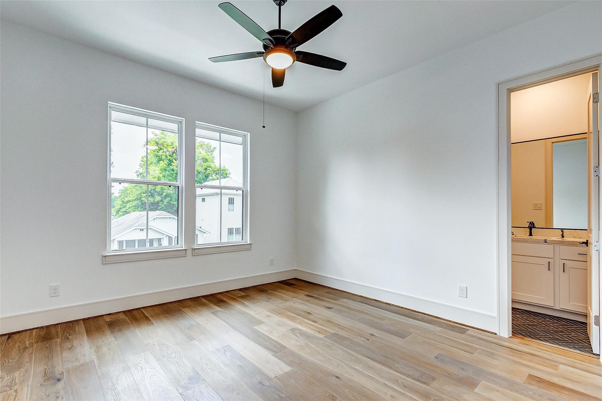 Bright bedroom with hardwood floors, large windows, and a ceiling fan, leading to an en-suite bathroom.