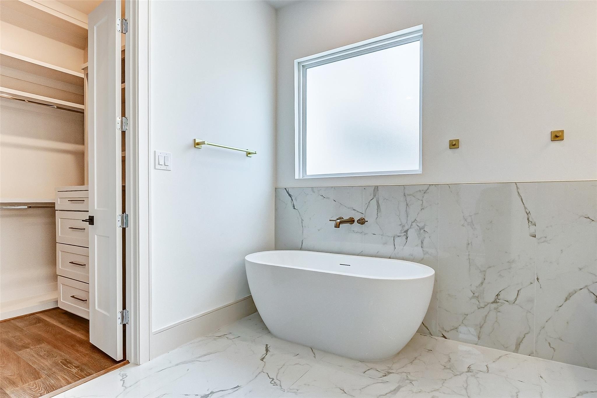 Large freestanding soaking tub beneath a window providing natural light without compromising privacy.
