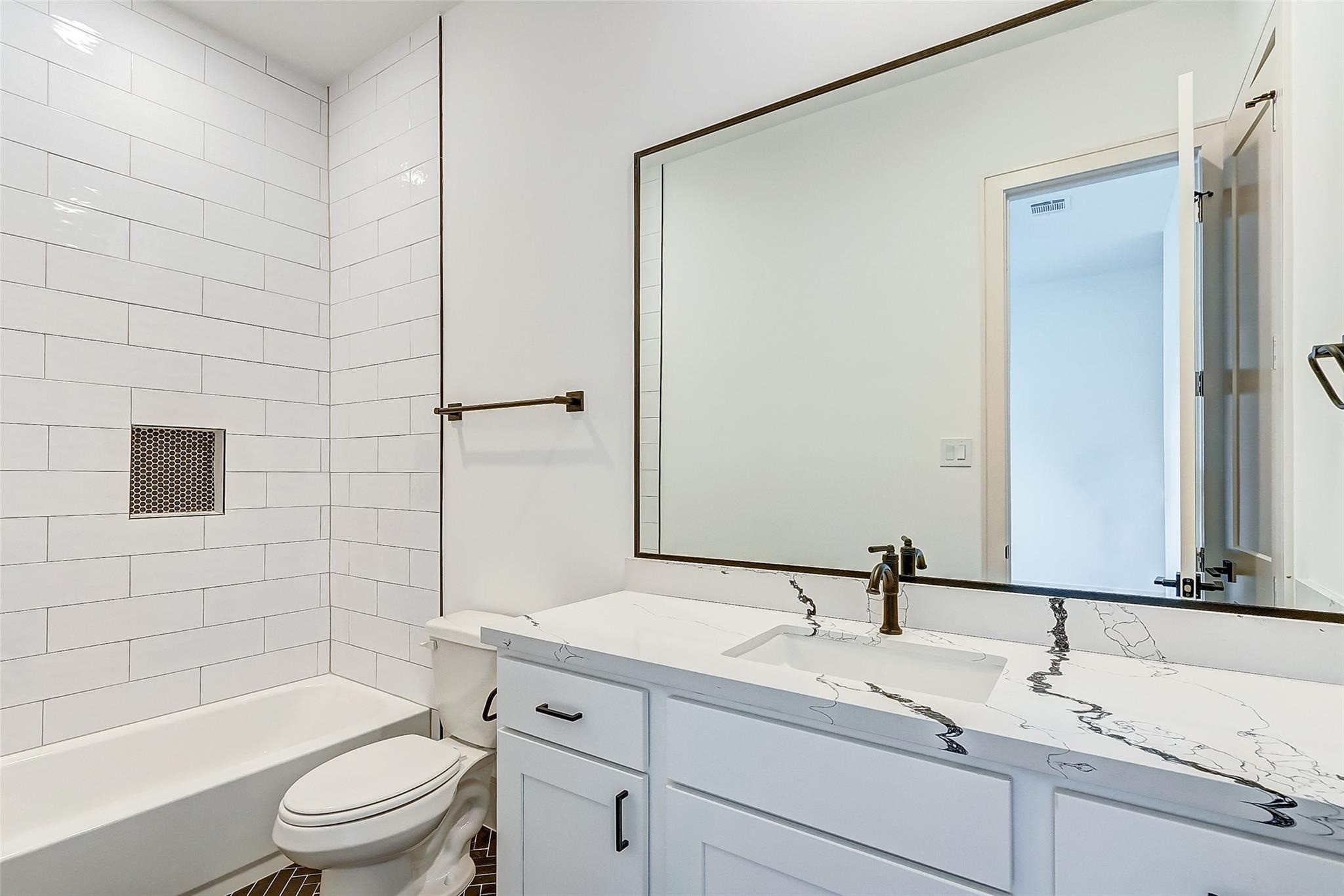 Modern bathroom featuring quartz  countertop, large mirror, elegant fixtures, and a stylish subway-tiled shower.