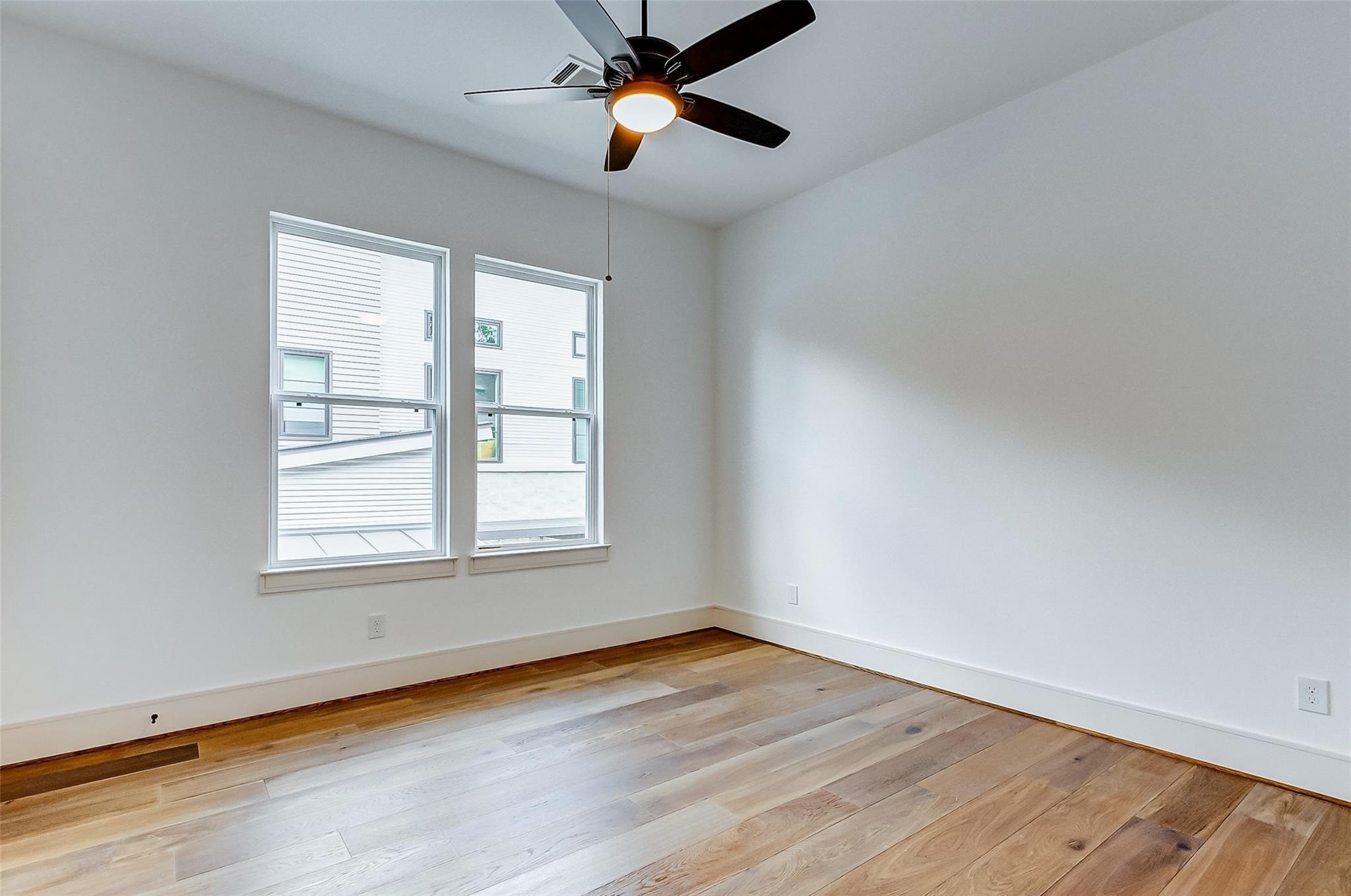 Bright and airy room with sleek hardwood flooring, modern ceiling fan, and large windows inviting natural light.