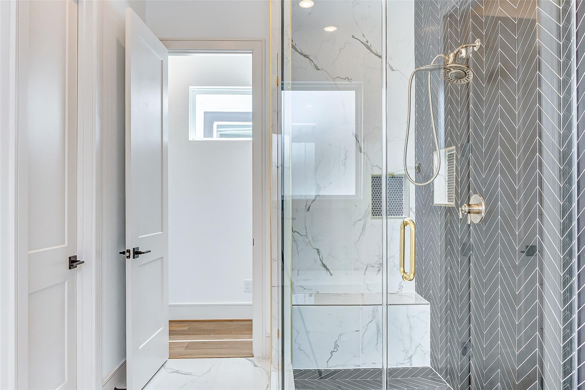 Frameless glass enclosed standing shower with herringbone tile and modern brass hardware.