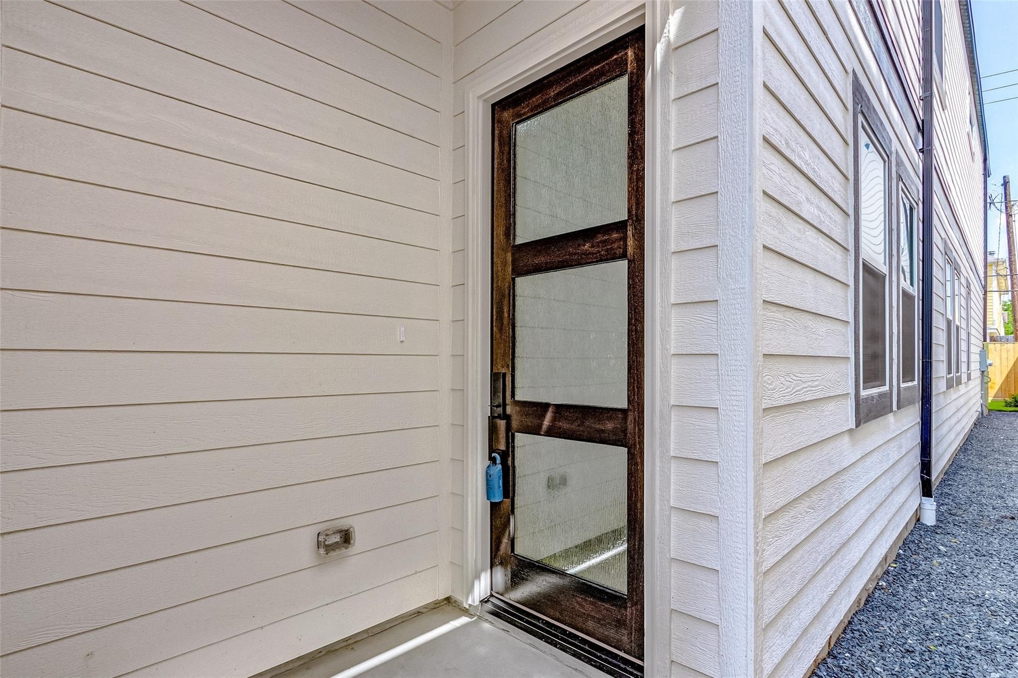 Inviting entryway featuring a sleek glass-paneled door, complemented by hardy plank siding, offering a welcoming and contemporary feel. Inviting entryway featuring a sleek glass-paneled door, complemented by hardy plank siding, offering a welcoming and contemporary feel.