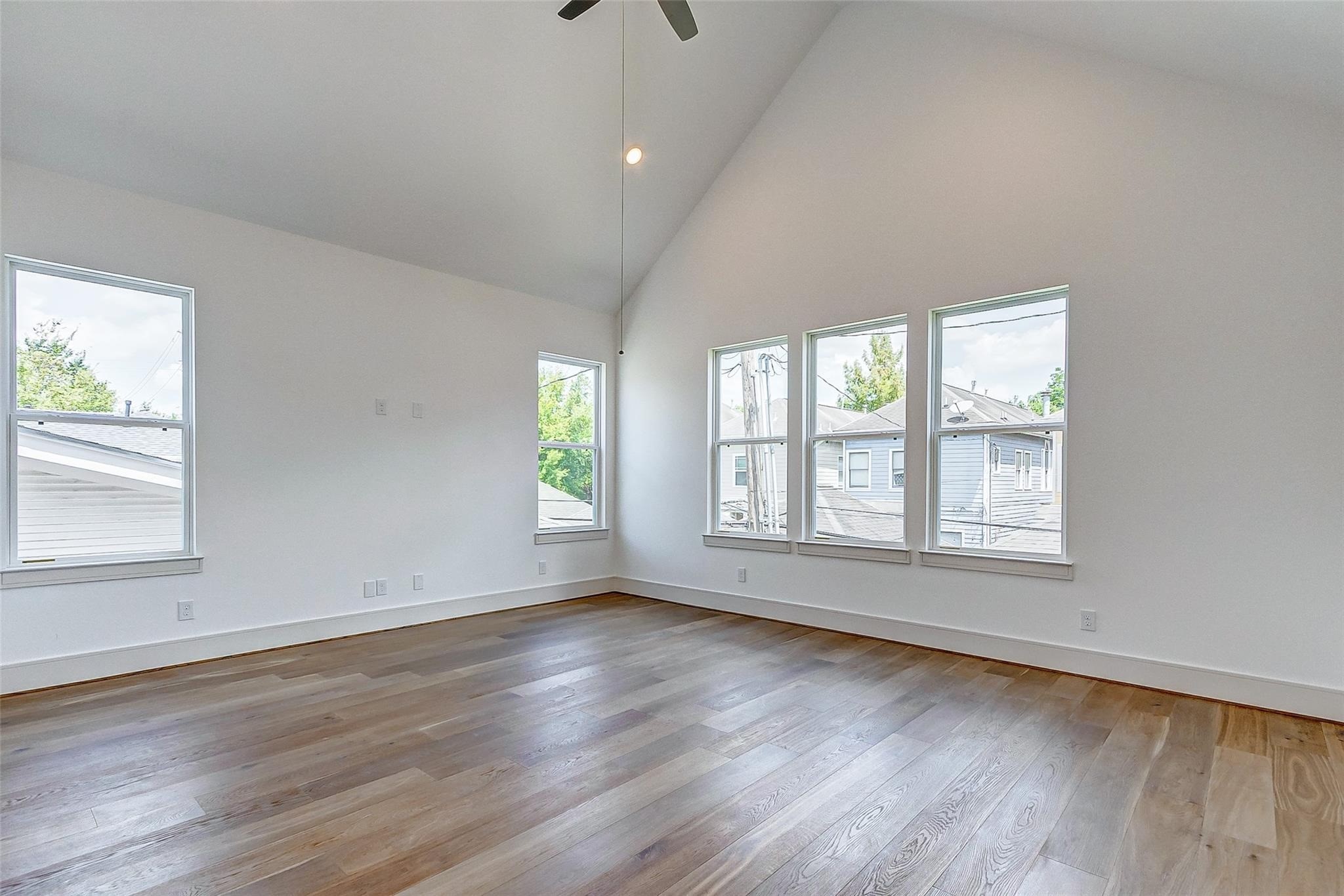 Spacious primary suite featuring high vaulted ceilings, abundant natural light through multiple windows, elegant hardwood flooring, and a stunning ensuite spa like bathroom.