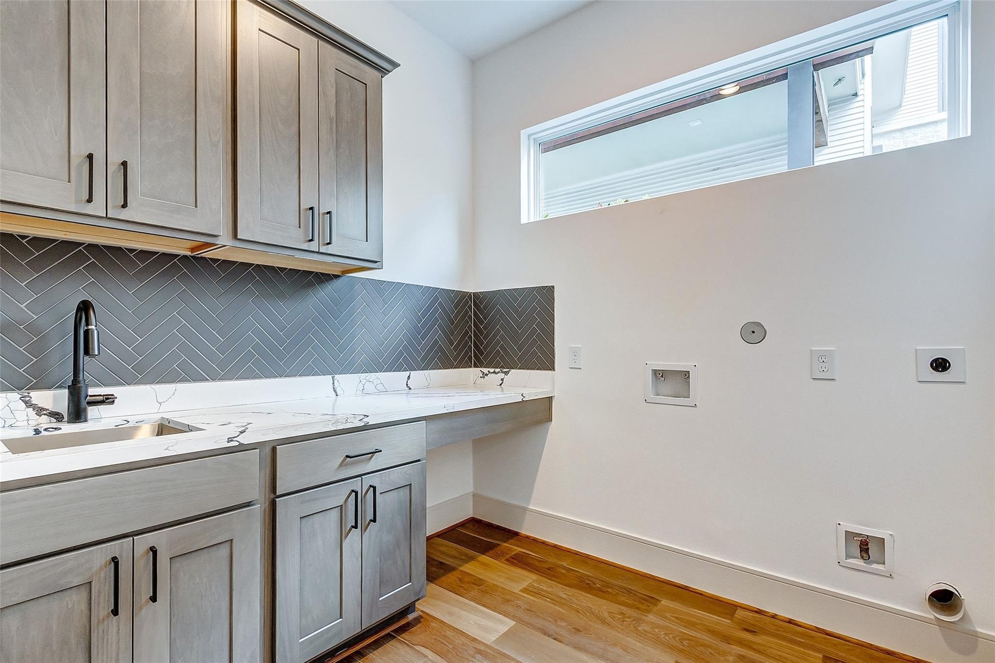 Chic laundry room featuring sleek cabinetry, a sink, modern herringbone backsplash, and a spacious countertop, complemented by ample natural light.
