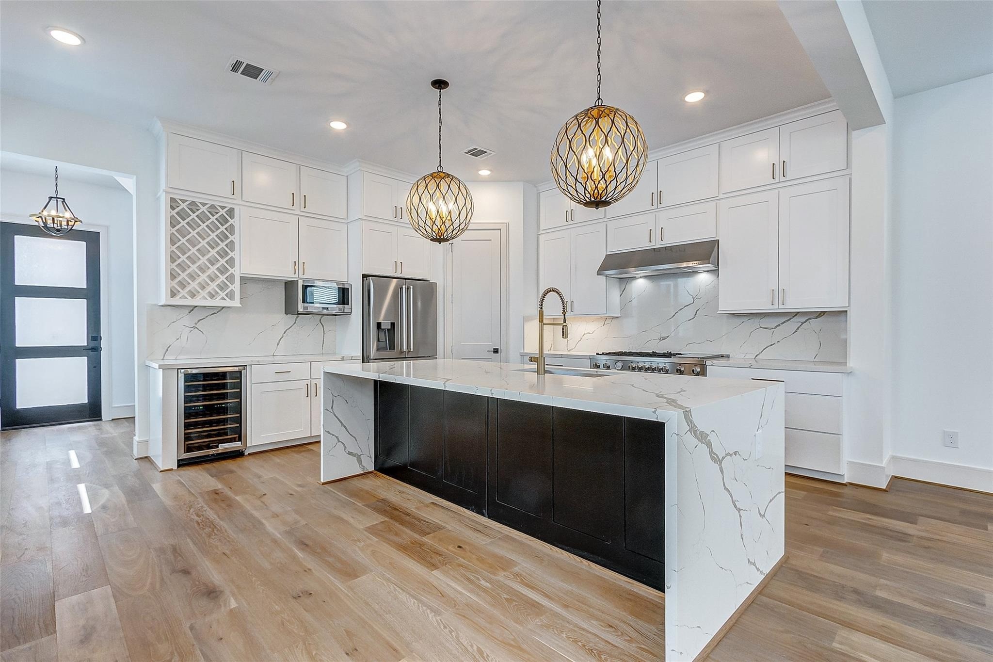 Experience luxury in this modern kitchen featuring a spacious island with elegant waterfall countertops and statement pendant lighting. High-end stainless steel appliances, a sleek wine cooler, and ample cabinetry provide style and functionality. Experience luxury in this modern kitchen featuring a spacious island with elegant waterfall countertops and statement pendant lighting. High-end stainless steel appliances, a sleek wine cooler, and ample cabinetry provide style and functionality.