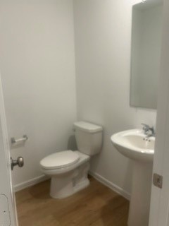 Charming half-bath featuring a modern pedestal sink, sleek mirror, and elegant wood flooring, perfect for guests.