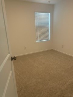 Cozy bedroom with soft carpeting and natural light streaming through a window with blinds, offering a clean and inviting space.