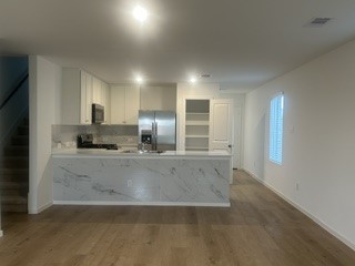 Modern kitchen with sleek marble countertops, stainless steel appliances, and open shelving, seamlessly flowing into the living area with hardwood floors.