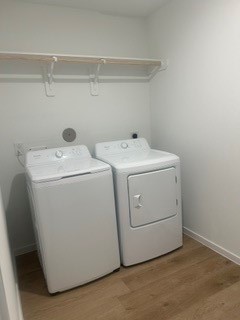 Bright laundry room featuring modern washer and dryer set, with convenient overhead shelving and sleek wood flooring.