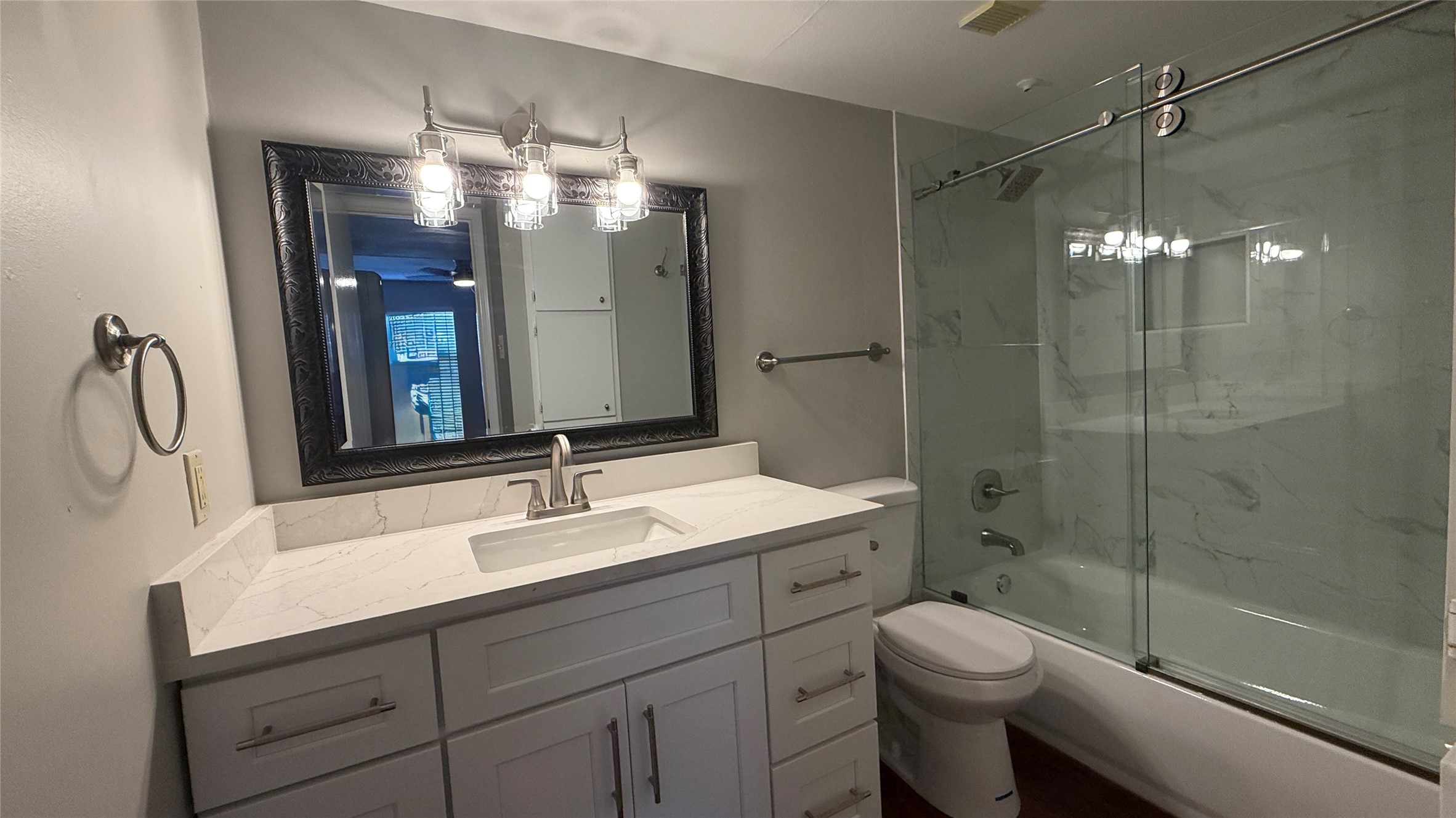 Updated bathroom featuring a spacious vanity, decorative mirror, modern lighting, and glass-enclosed tub/shower combination.