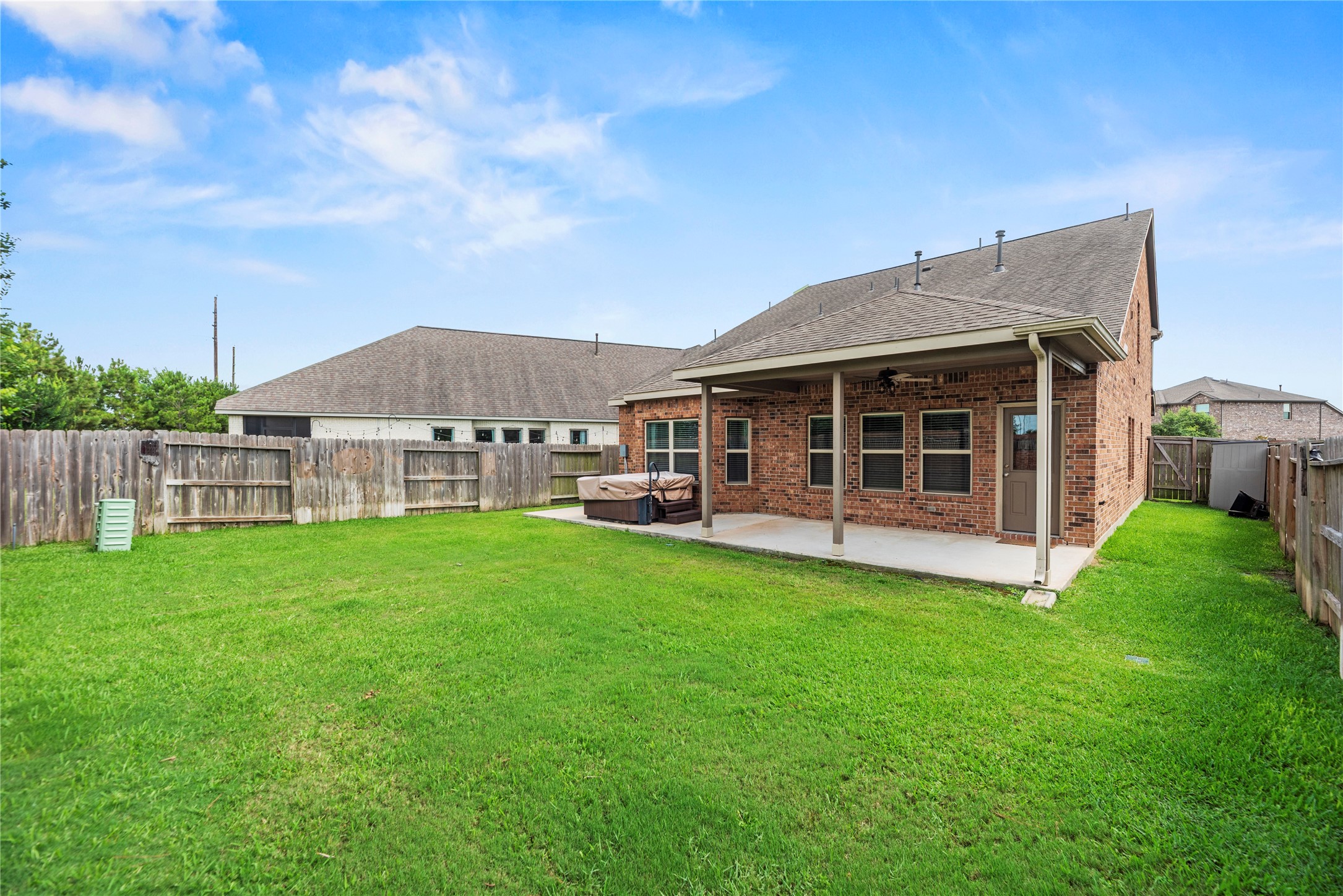 This rear view underscores the scope of the fully fenced yard, highlighted by a professional underground sprinkler system and a dedicated, built-in outdoor spa/hot tub.