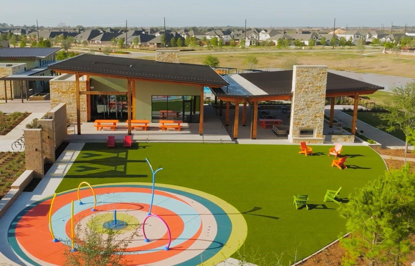 A vibrant outdoor gathering space in Elyson designed for everyday enjoymentfeaturing an interactive splash pad, open green space for play and relaxation, and shaded seating areas perfect for meeting neighbors and enjoying Katys sunny Texas days.