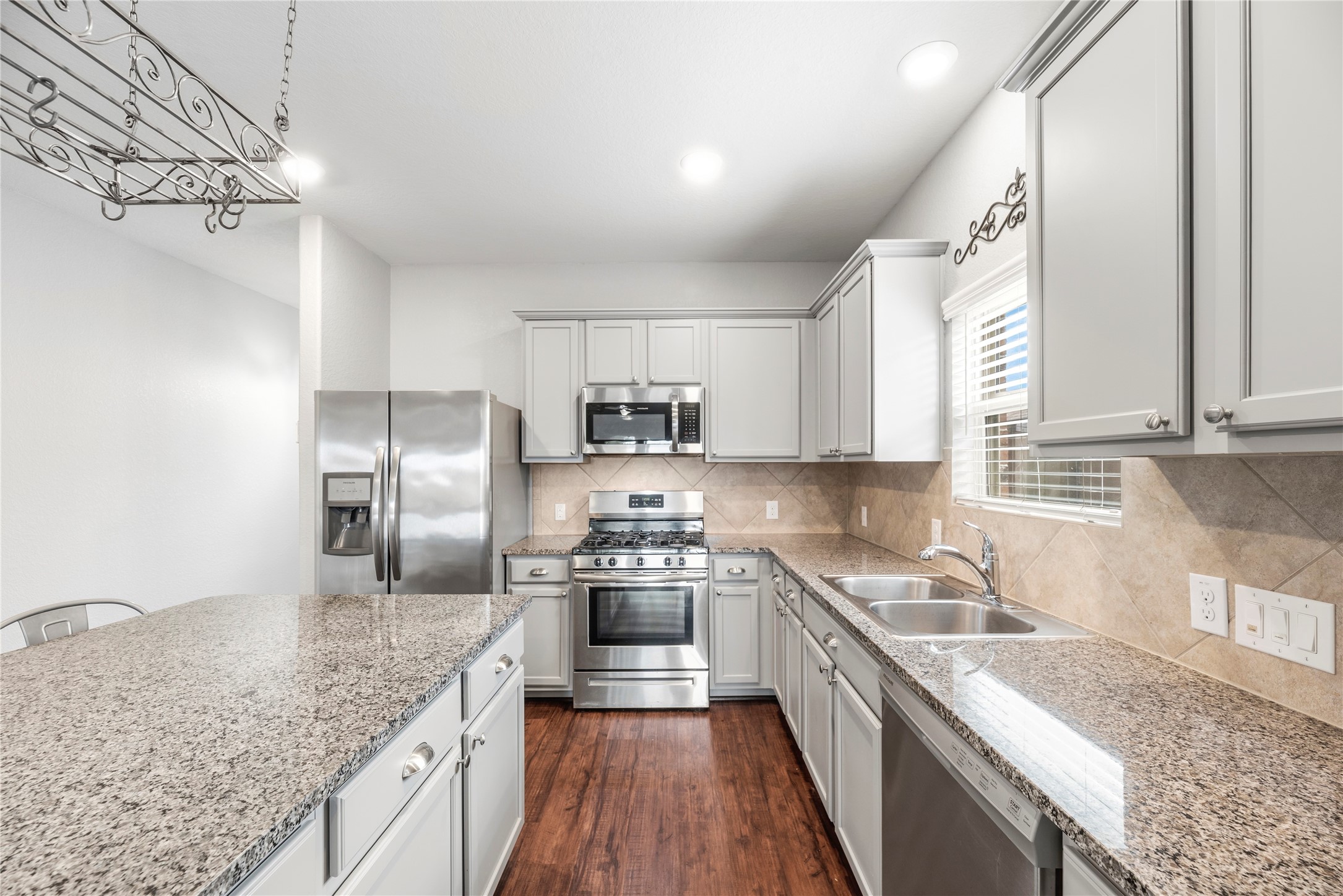 Another angle of the beautifully appointed kitchen reveals timeless tile backsplashes, a deep double-bowl stainless sink positioned under a bright window, under-cabinet lighting, and a layout carefully designed to maximize prep space.