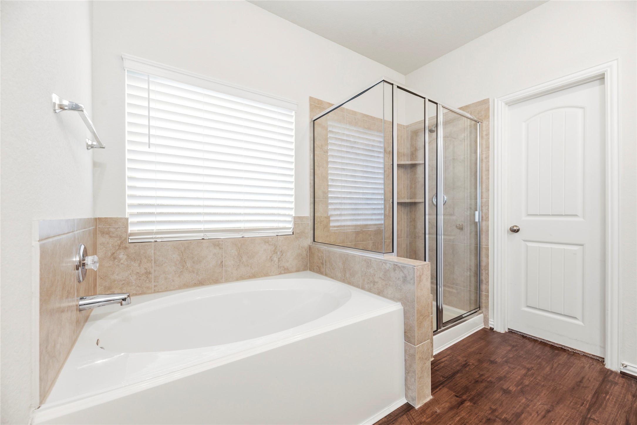 The spa-like configuration of the primary bath features a deep, integrated corner soaking tub nestled beneath a large window, paired with a dedicated glass-enclosed walk-in shower stall lined in timeless tile.