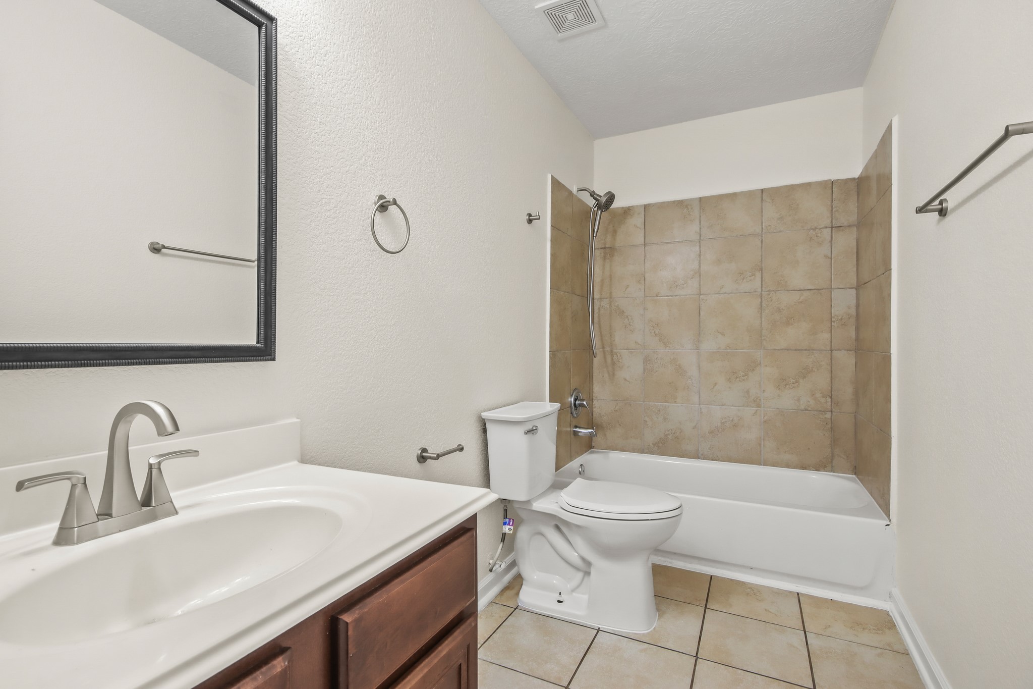 Secondary bathroom featuring granite countertops and backsplash, tile floors, a framed mirror, and a shower/tub combo.