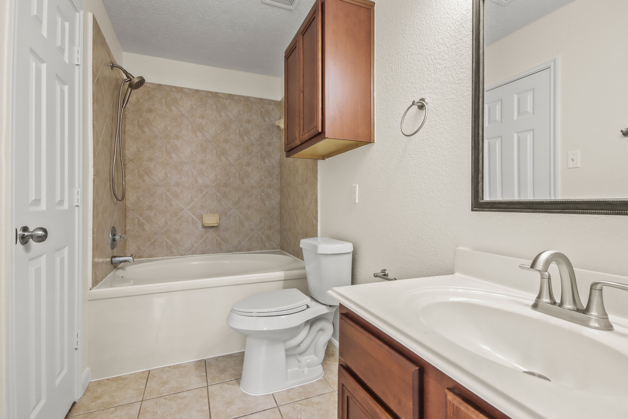 The master bathroom features warm wood cabinetry paired with sleek countertops, a framed mirror, and a convenient shower/tub combination, offering both style and functionality. It is complete with a spacious built-in closet.