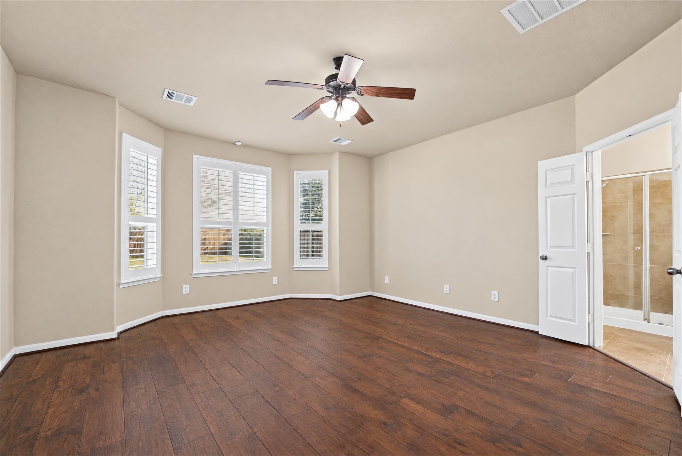 Elegant, large primary bedroom. Note the beautiful engineered wood floors and plantation shutters on all windows!  French doors lead into the primary bathroom.