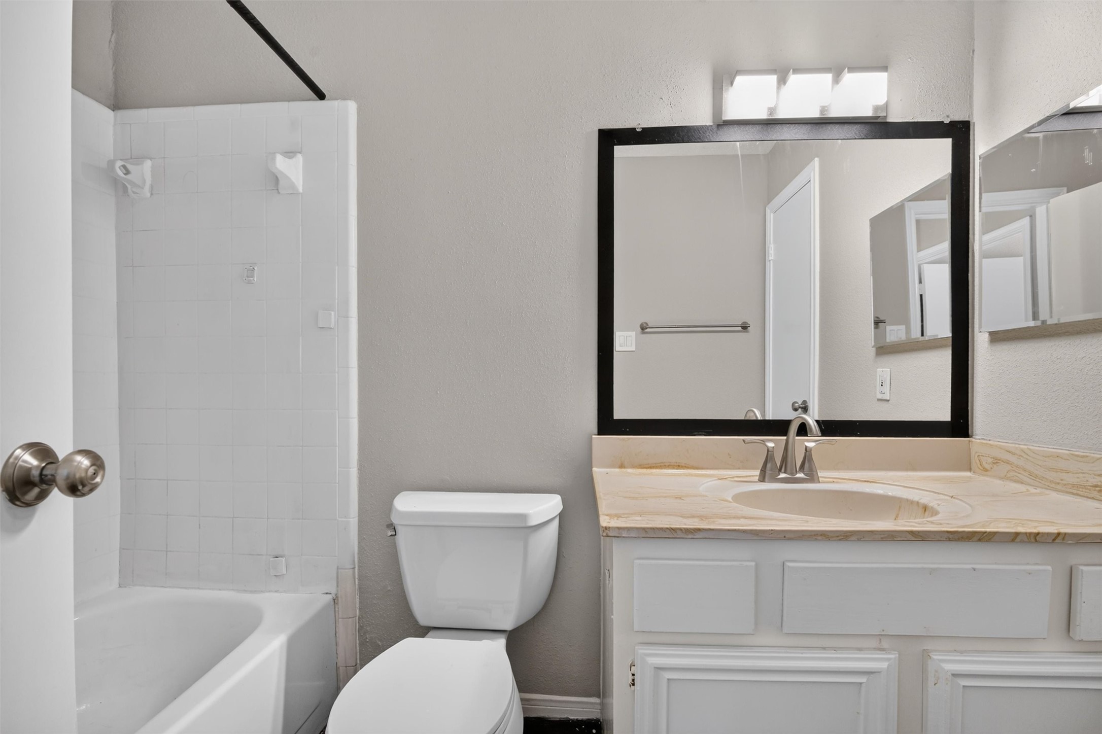 Secondary full bathroom with a tub and shower combination, vanity storage, and a framed mirror.