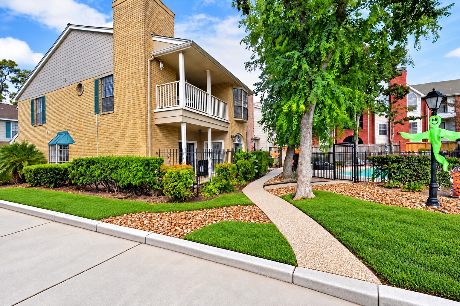 Inviting exterior with a covered balcony, mature trees, and landscaped grounds beside the community pool.