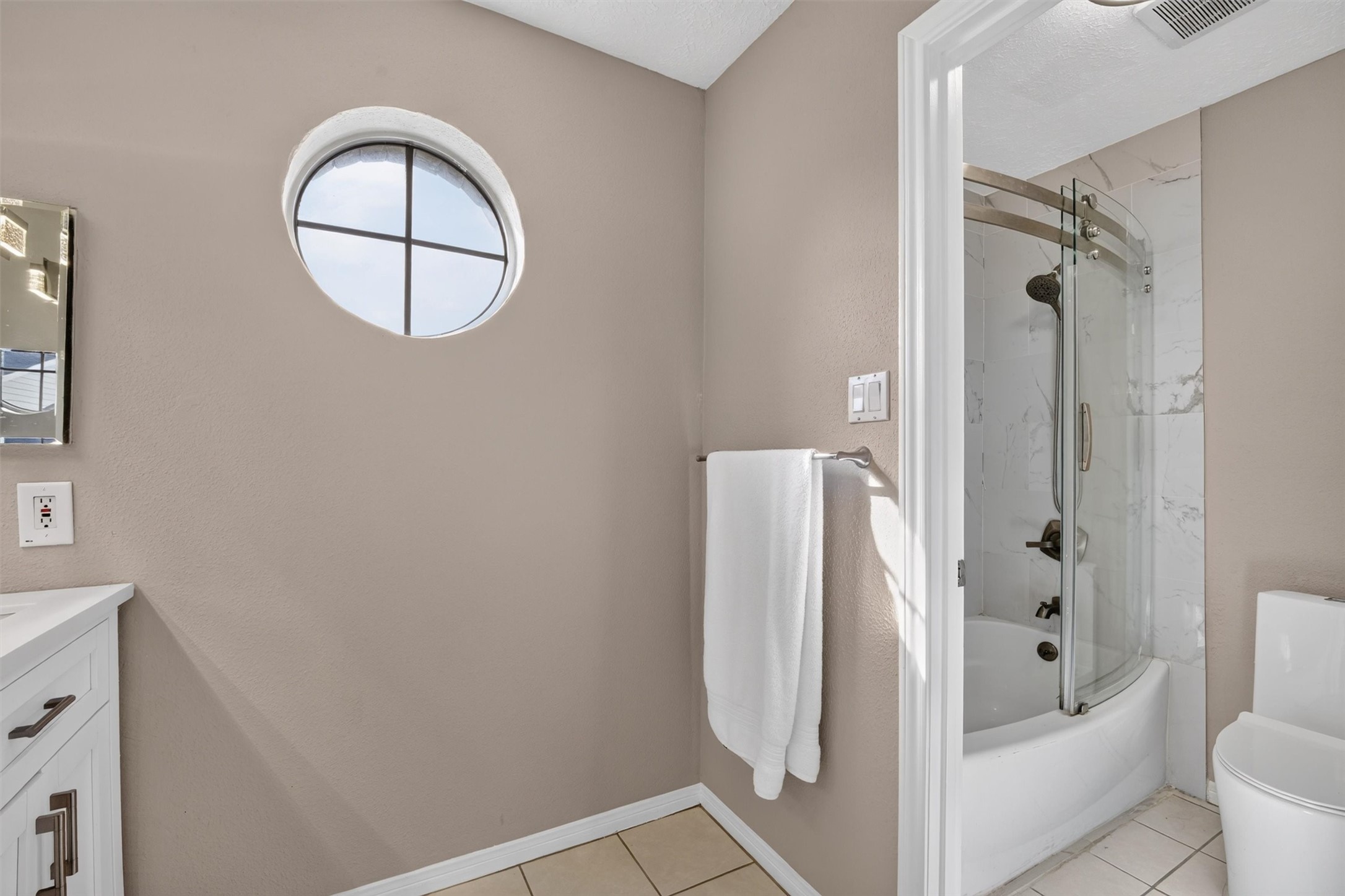 Primary bathroom featuring a glass-enclosed shower and a distinctive round window.