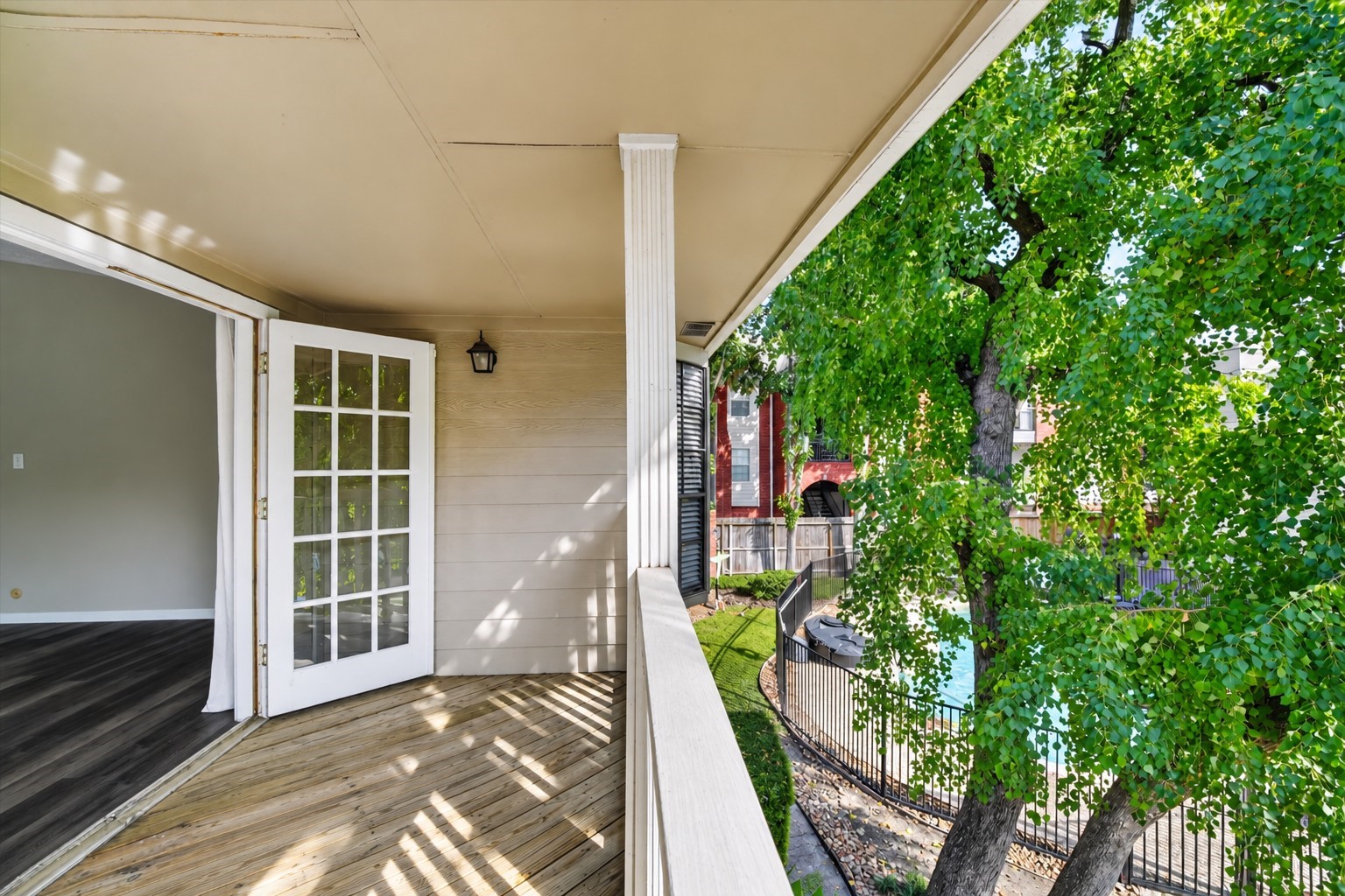 Covered balcony off the primary suite, overlooking mature trees and the community poola relaxing retreat for morning coffee or unwinding outdoors.