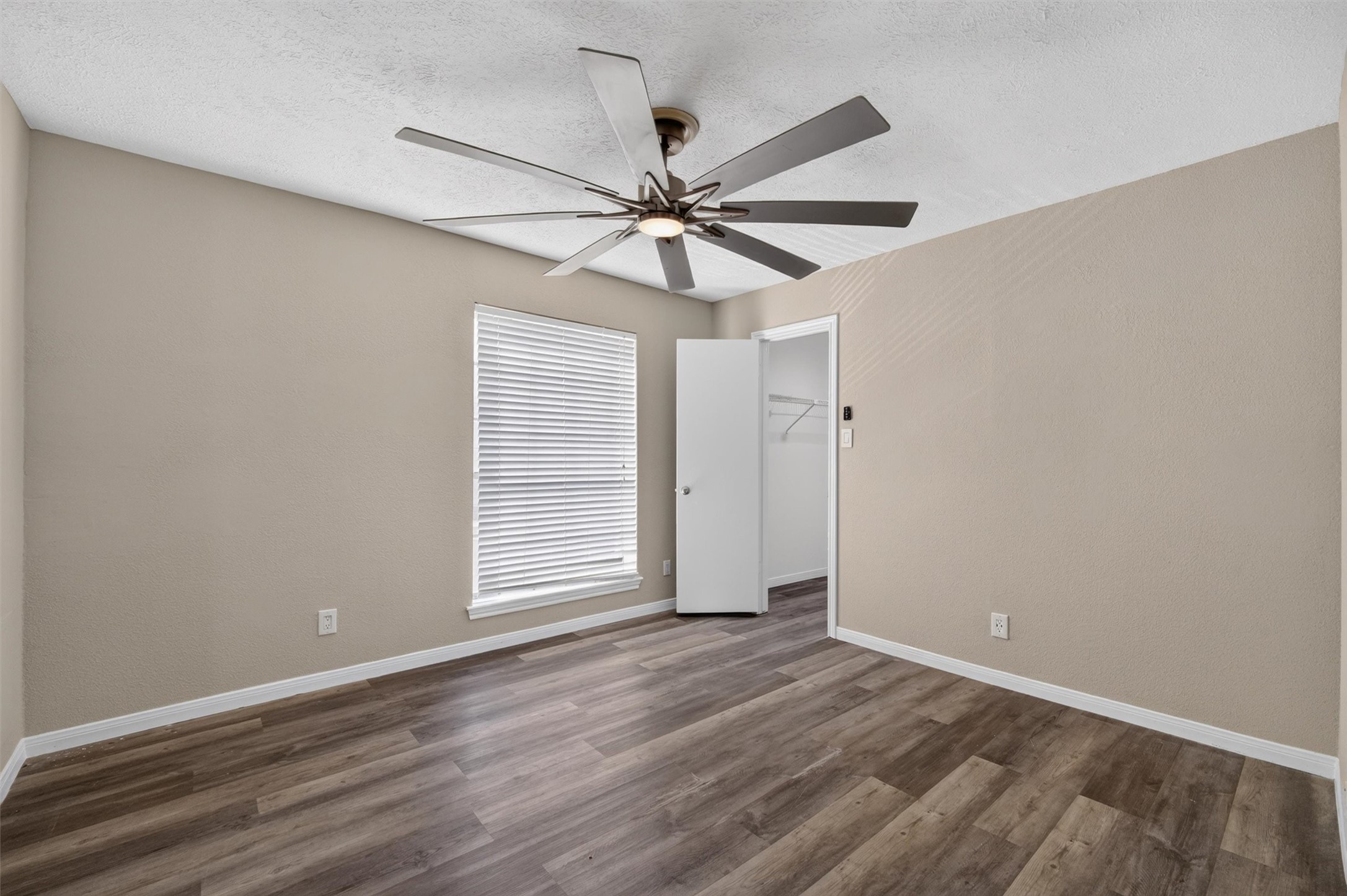 Unstaged additional bedroom showing its layout, ceiling fan, and wood-look flooring.