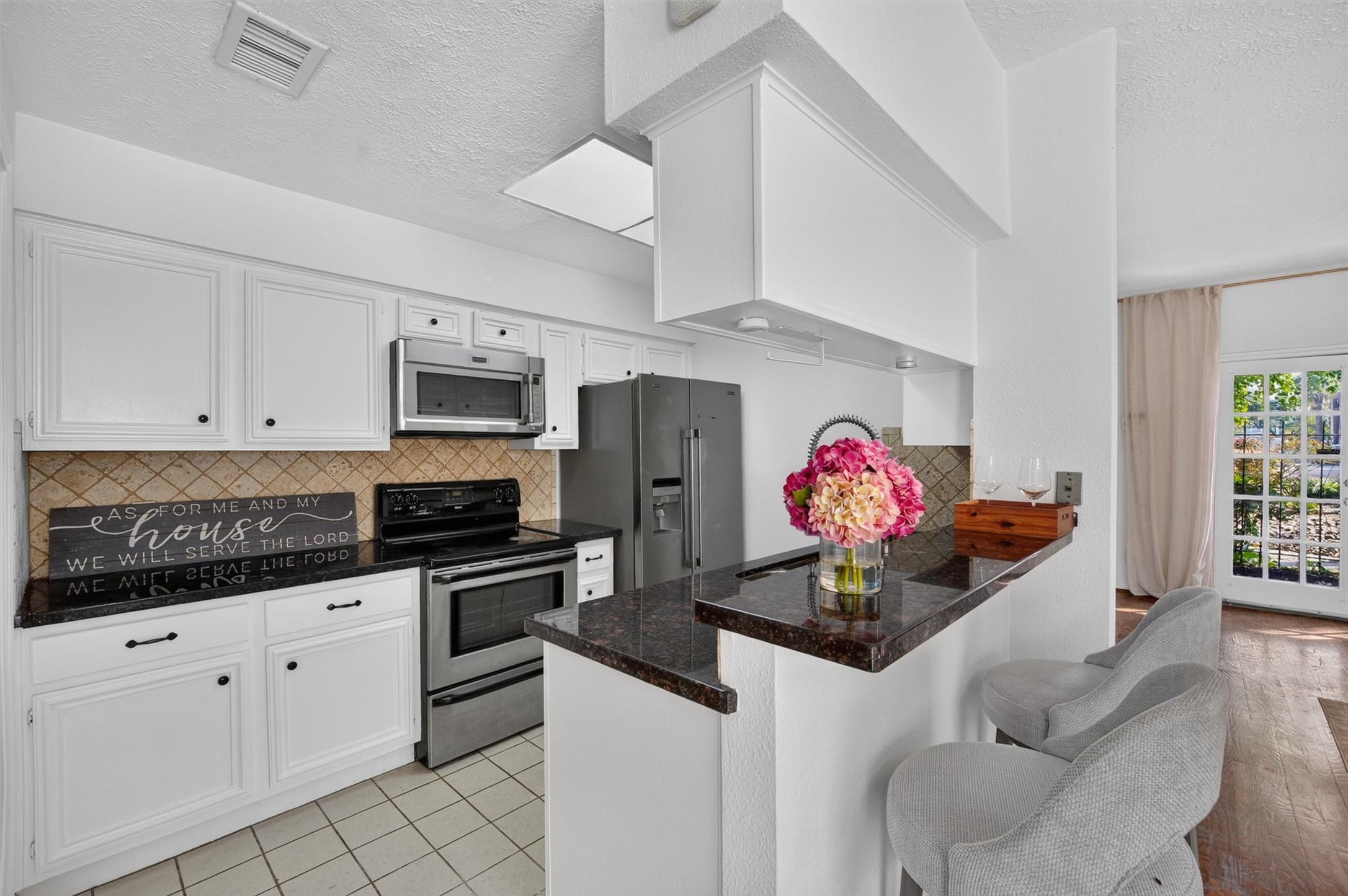 Kitchen featuring white cabinetry, dark countertops, stainless steel appliances, and breakfast bar seating.