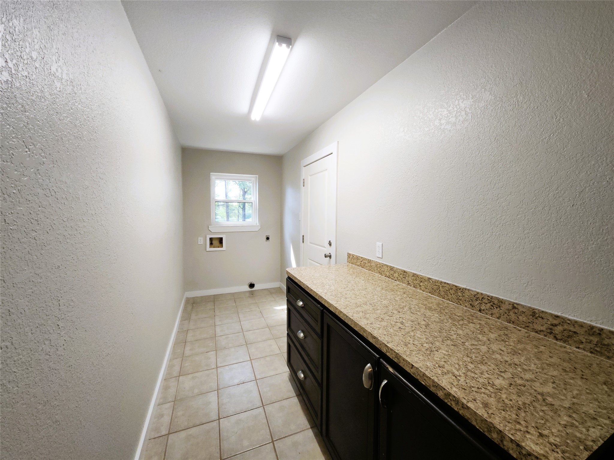Spacious laundry room with ample counter space, sleek cabinetry, and natural light through the window, offering functionality and style.