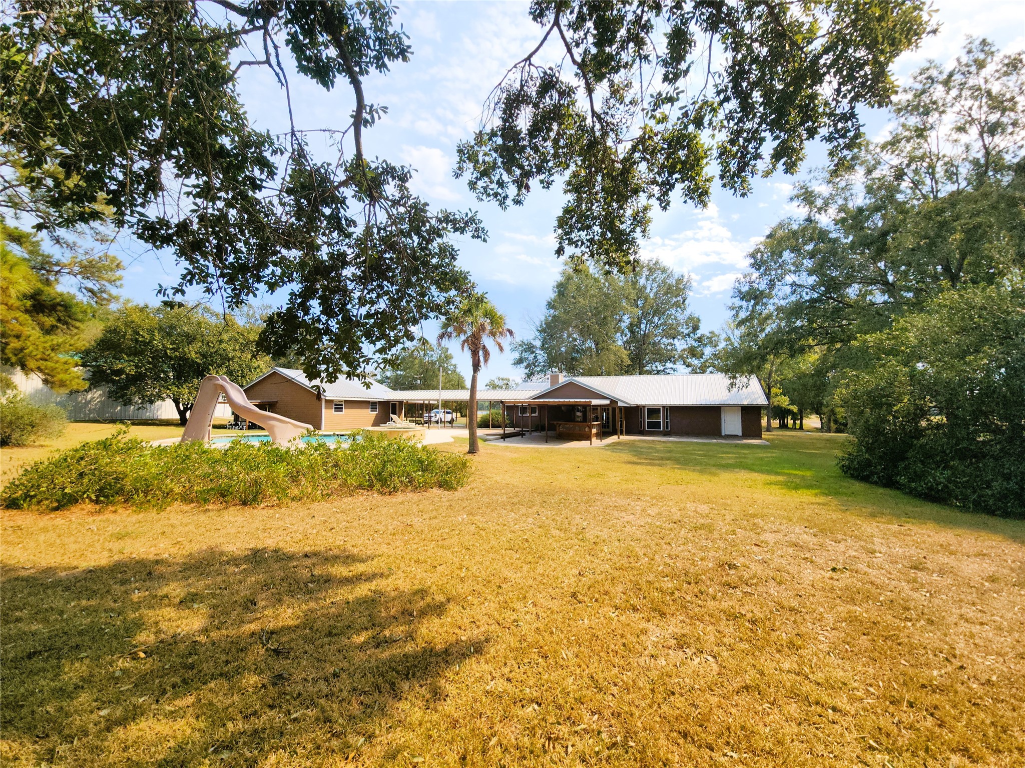 A view of the backyard, showing the pool, back of the house with covered walk-way over to the detached 3-car garage.