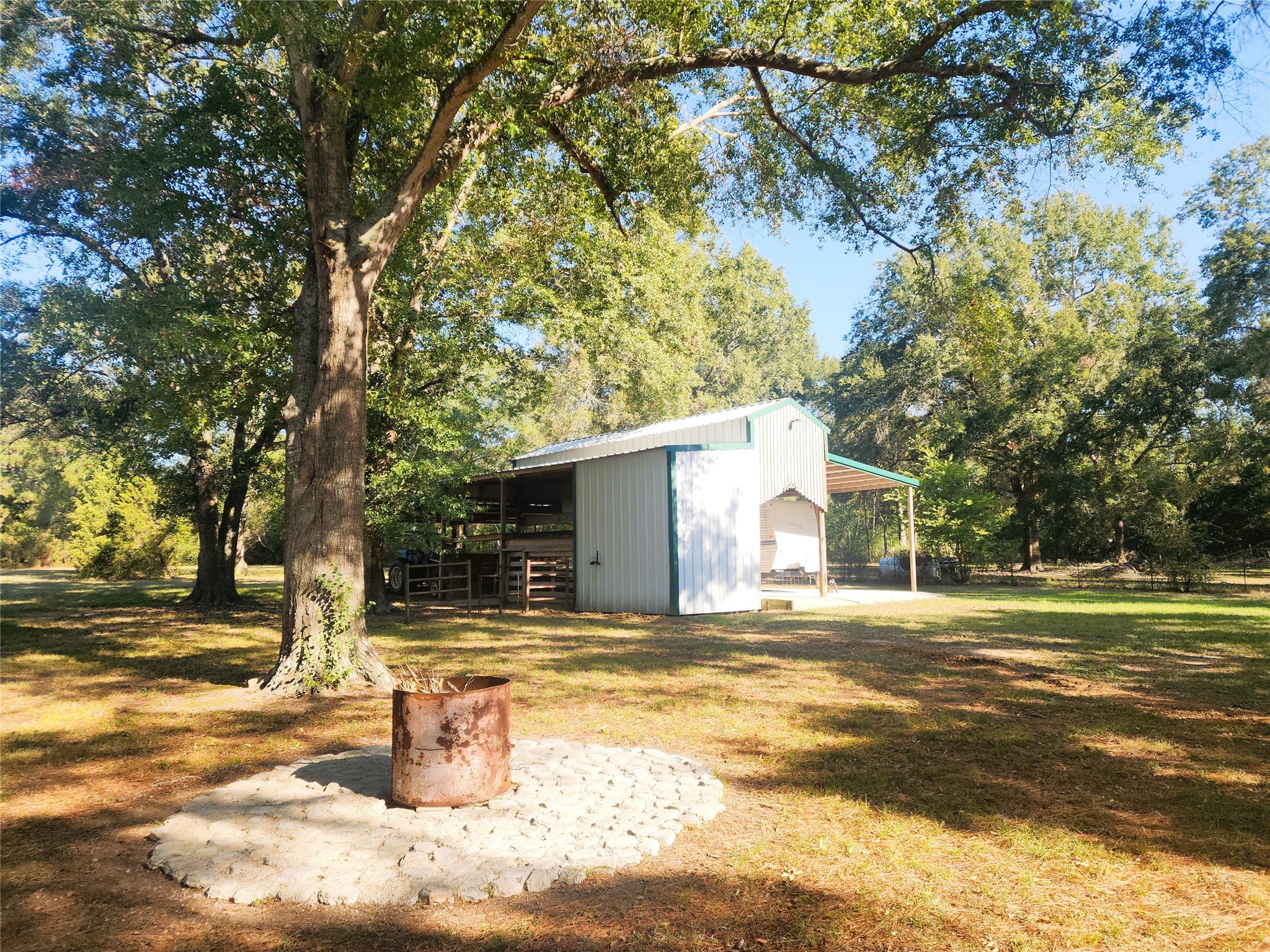 Expansive outdoor area featuring a rustic fire pit surrounded by mature trees, offering a perfect setting for gatherings and relaxation.