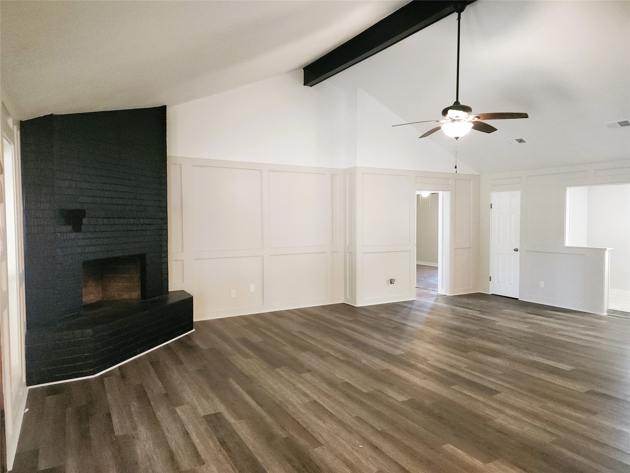 Spacious living room featuring a striking black brick fireplace, vaulted ceilings with exposed beams, and elegant wood-look flooring for a modern and inviting atmosphere. Spacious living room featuring a striking black brick fireplace, vaulted ceilings with exposed beams, and elegant wood-look flooring for a modern and inviting atmosphere.