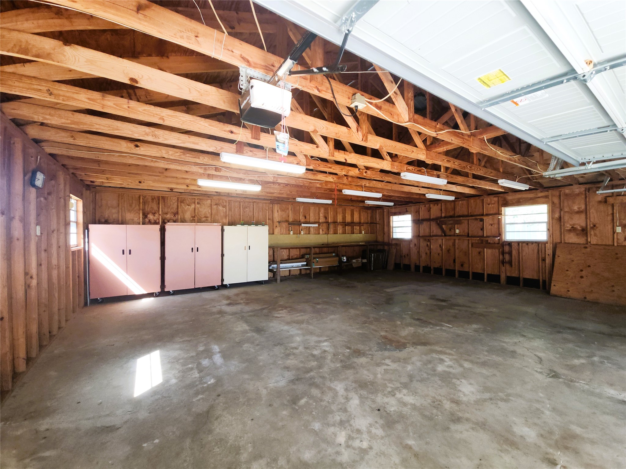 Spacious garage with ample natural light, featuring exposed beams and storage cabinets, perfect for projects and extra storage.