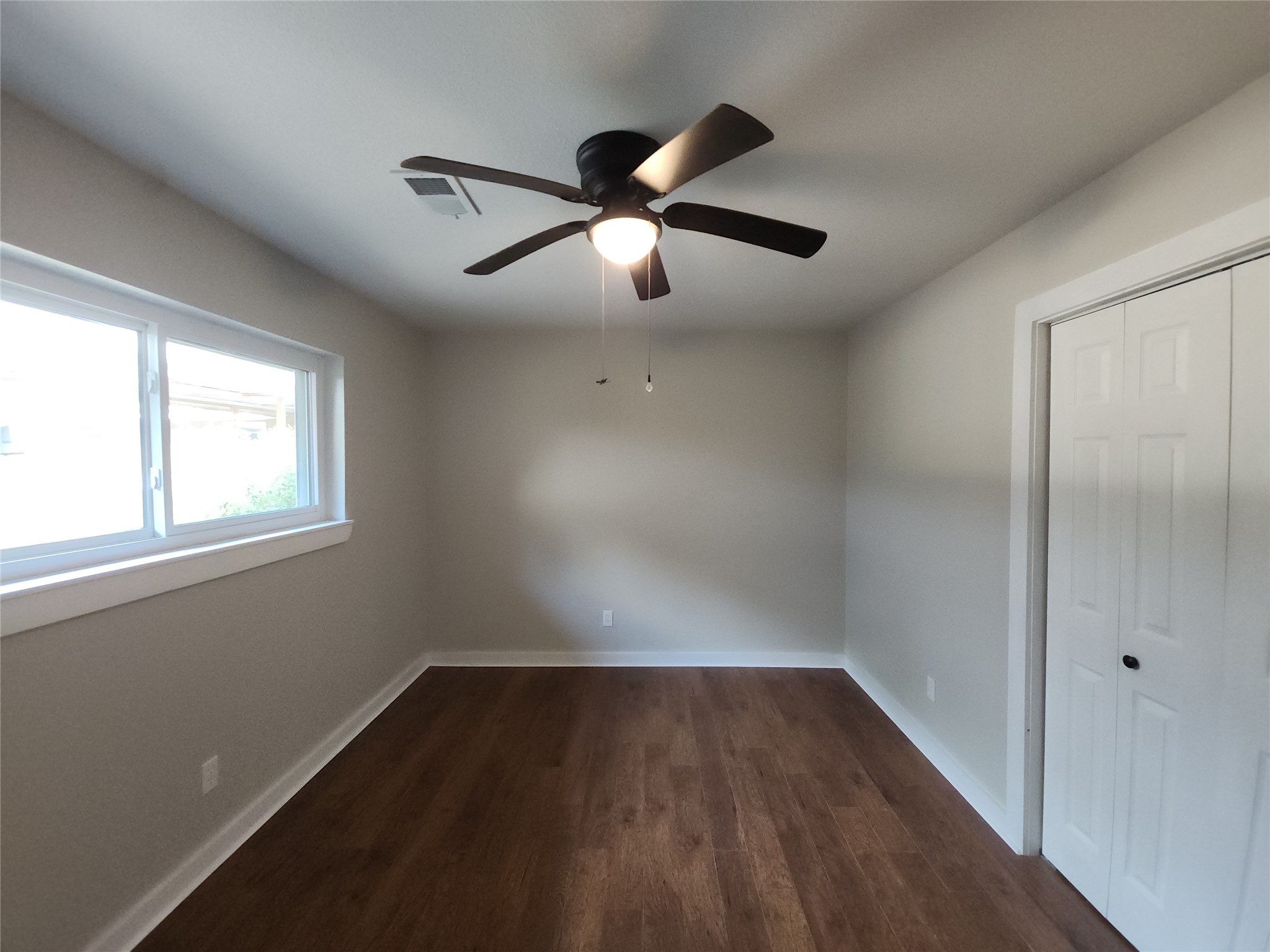 Bright and inviting bedroom featuring sleek flooring, a modern ceiling fan, ample natural light from a large window, and convenient closet space.