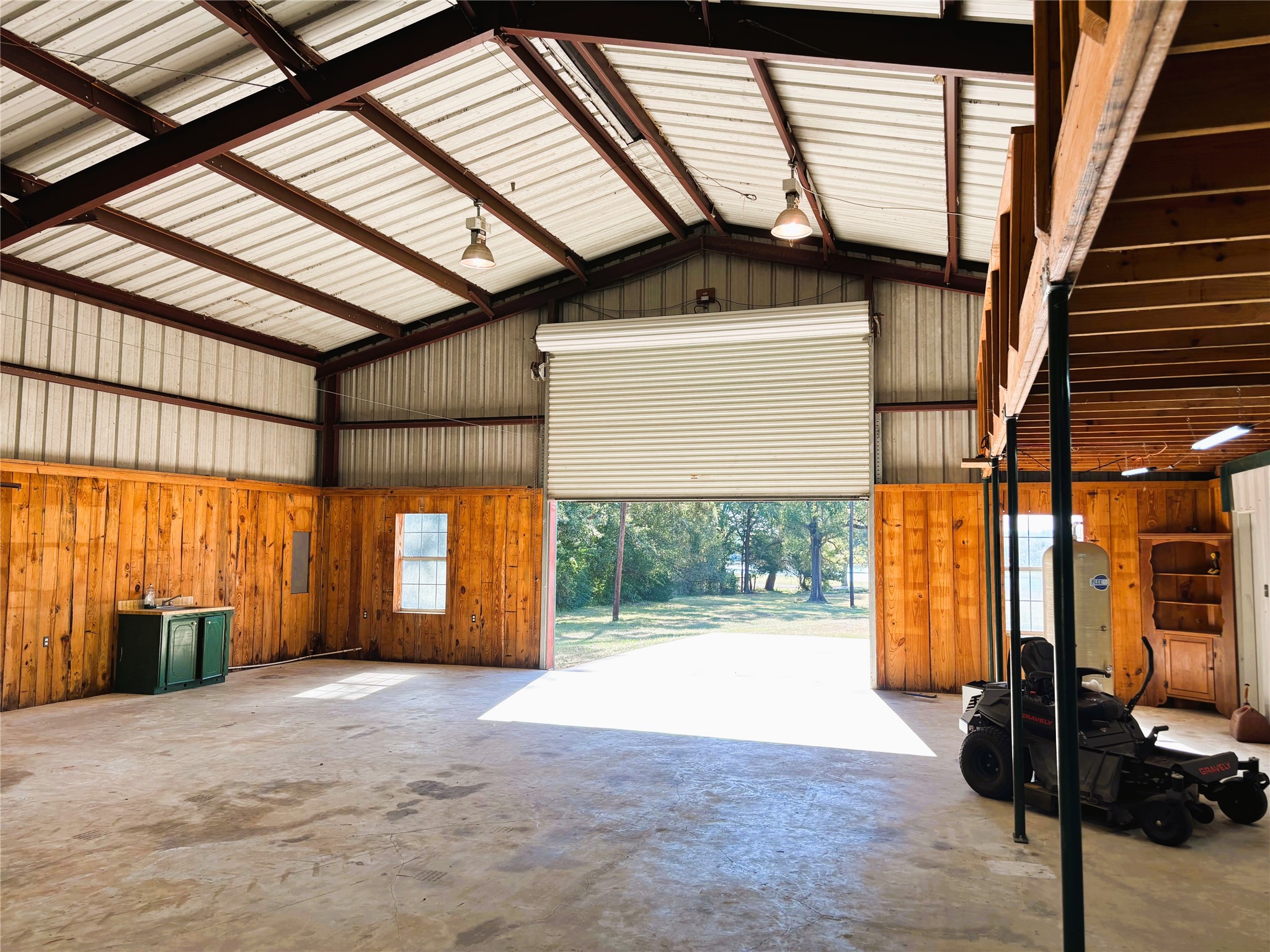 Spacious metal workshop with high ceilings, roll-up garage door, and natural light, perfect for projects or storage.