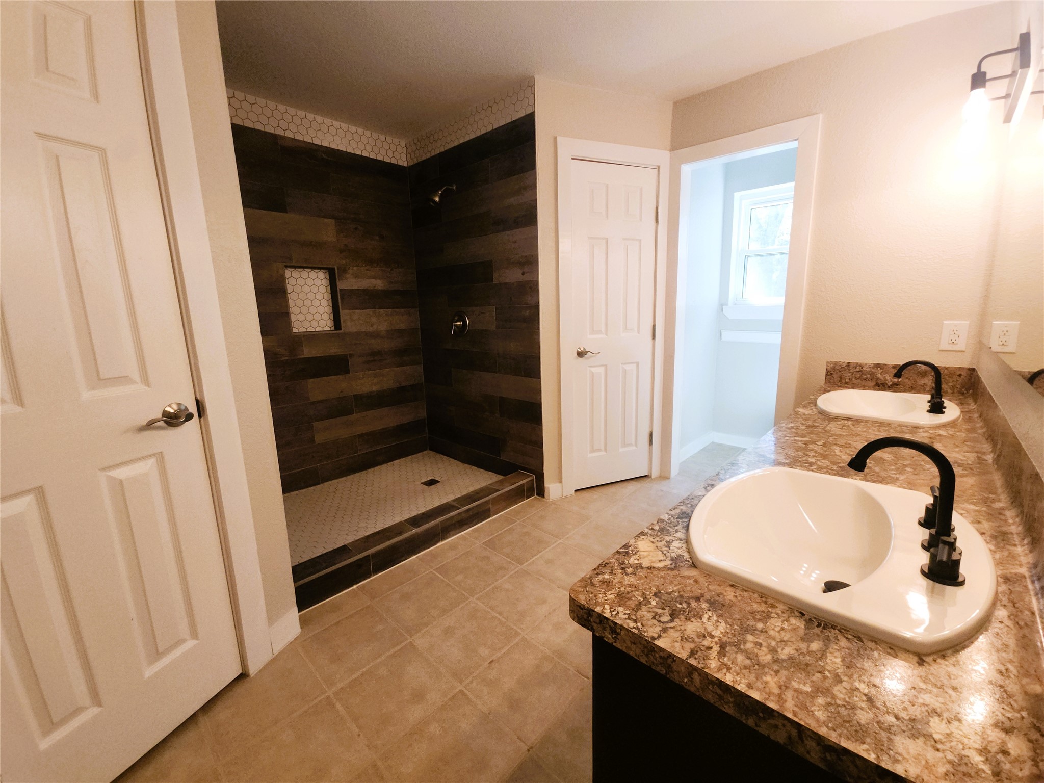 Spacious bathroom featuring a modern walk-in shower with stylish wood-look tile, dual sinks with elegant fixtures, and ample lighting.