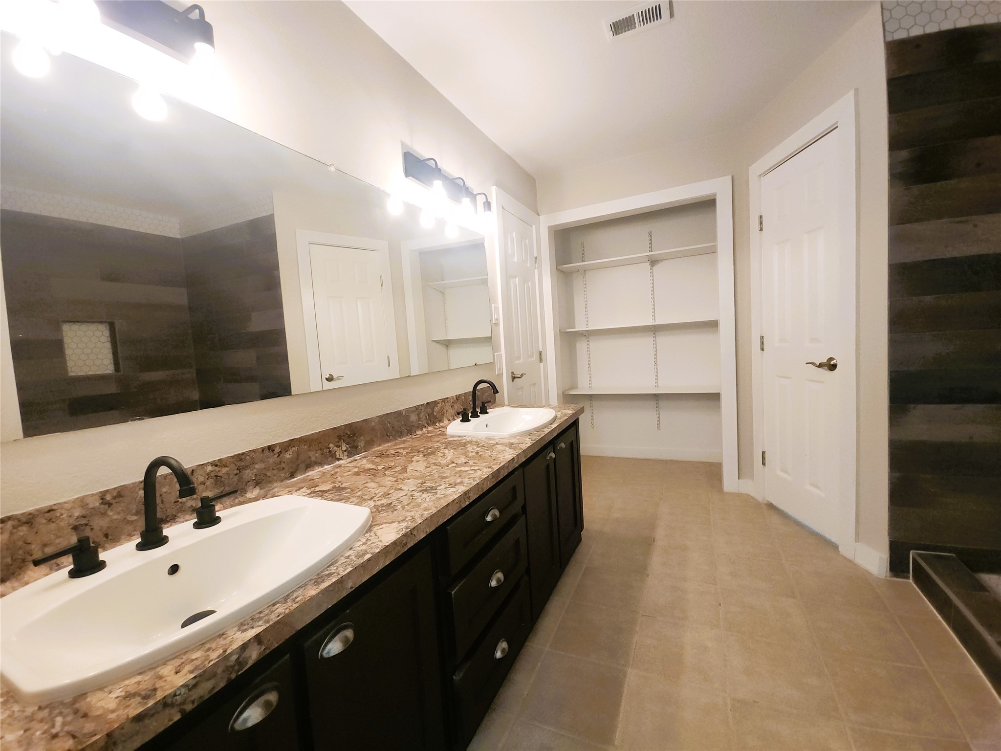 Spacious bathroom featuring a dual-sink vanity with ample open shelving, and sleek modern fixtures.