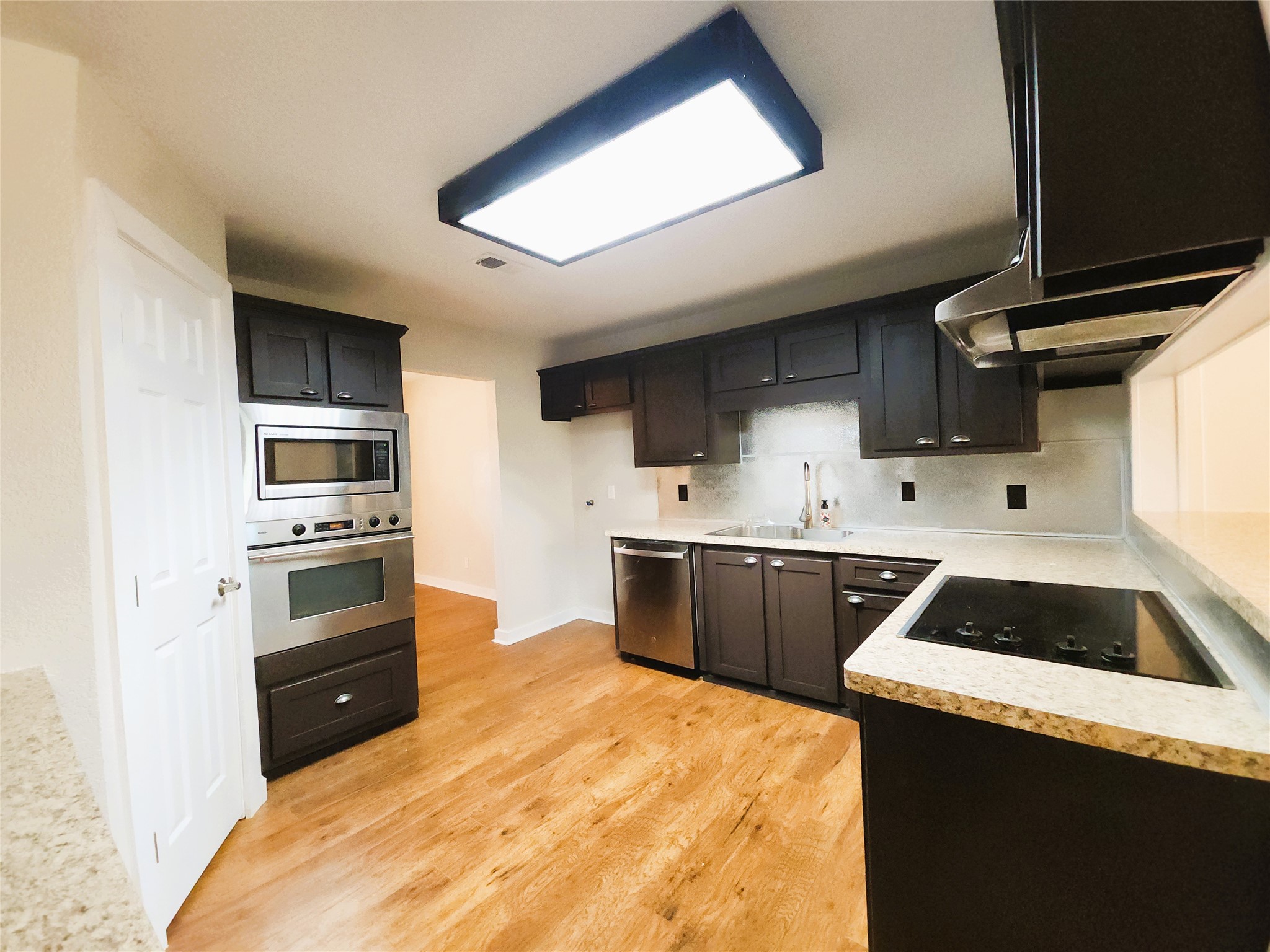 Kitchen with sleek dark cabinetry, stainless steel appliances, and warm wood flooring, providing a functional and stylish cooking space. Kitchen with sleek dark cabinetry, stainless steel appliances, and warm wood flooring, providing a functional and stylish cooking space.