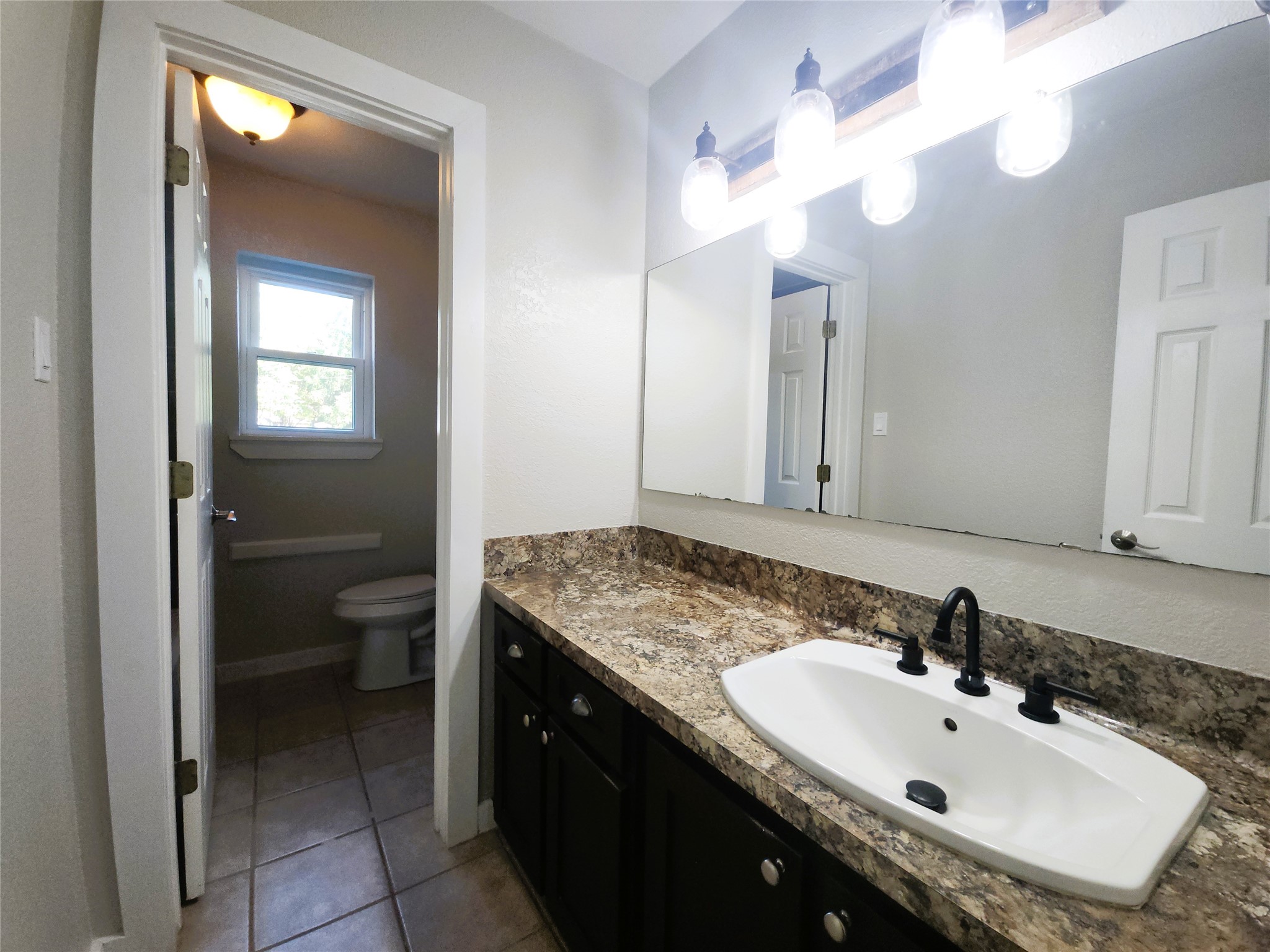 Secondary bathroom featuring a spacious vanity with a modern sink, complemented by stylish lighting and ample natural light from the adjacent window.