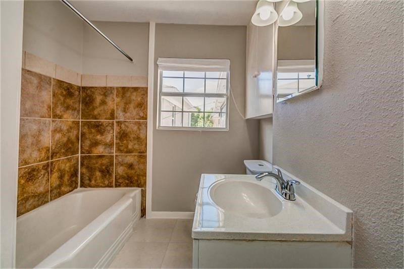 Bright bathroom with a tiled tub-shower combo, modern vanity, and ample natural light from the window.