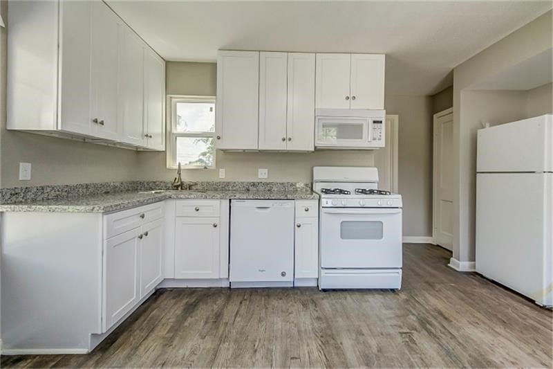 Kitchen with sleek white cabinetry, modern appliances, and elegant granite countertops, complemented by stylish wood-look flooring.