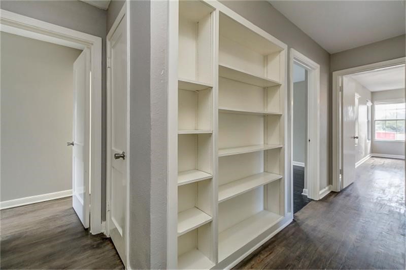 Hallway with built-in shelving, leading to spacious rooms with ample natural light and hardwood floors.