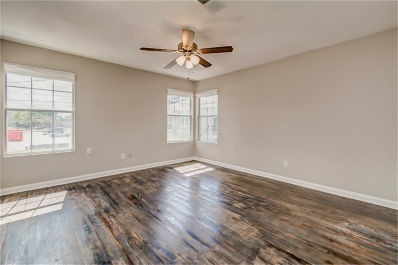 Room with rich hardwood floors, abundant natural light from multiple windows, and a ceiling fan for comfort.