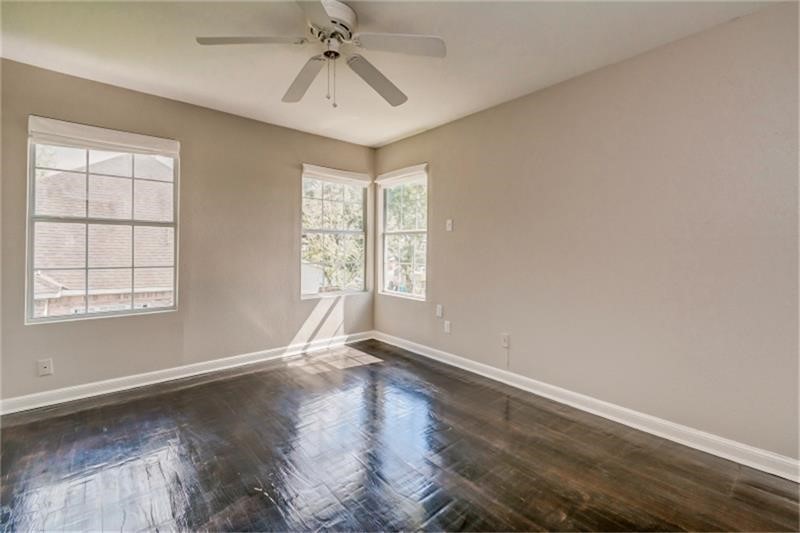 Bright and airy bedroom with gleaming hardwood floors, large windows, and a ceiling fan, offering a serene and inviting atmosphere.