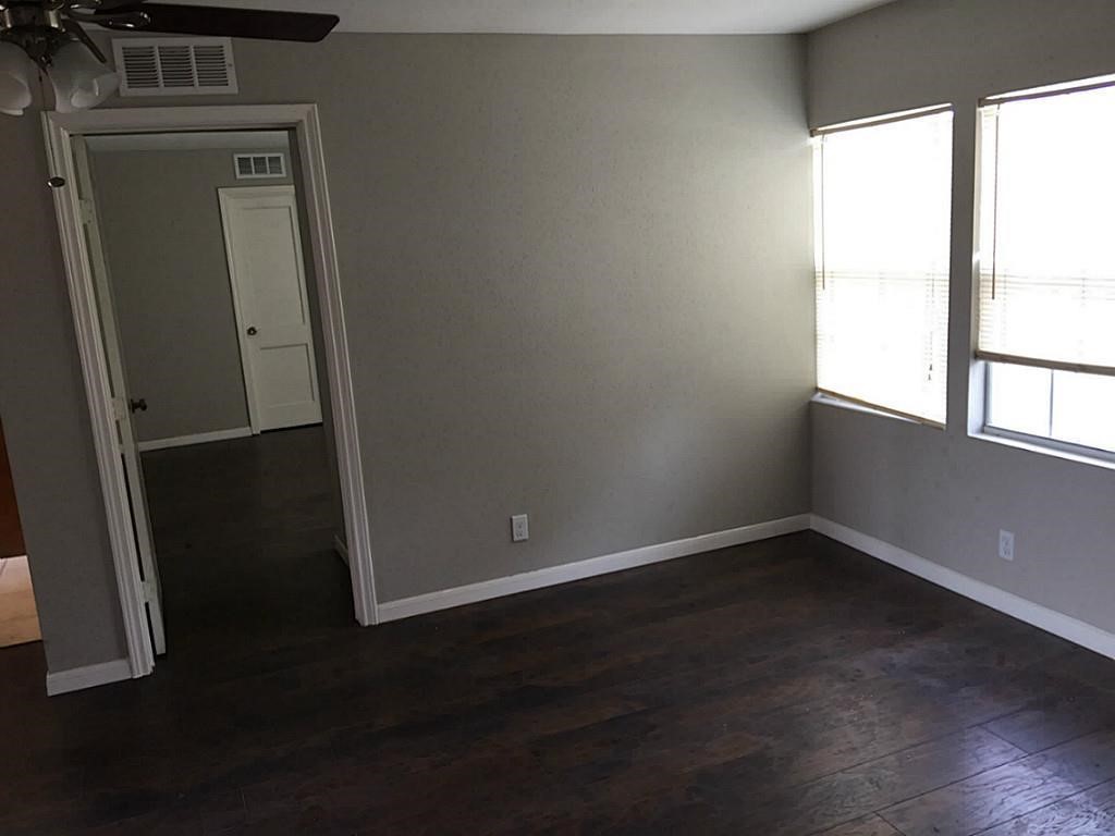 Room with dark hardwood floors, neutral walls, and ample natural light from large windows, offering a welcoming and versatile space.