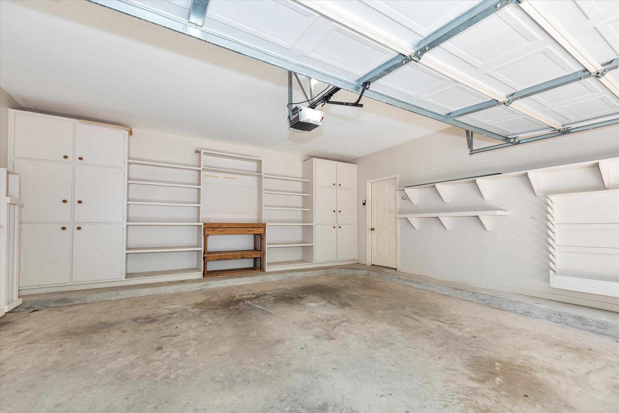 A view of this spacious and useful garage with multiple built-ins, shelves, a workbench, and an automatic garage door opener. It even has a billiard table cue stick holder for those that love the game of pool!