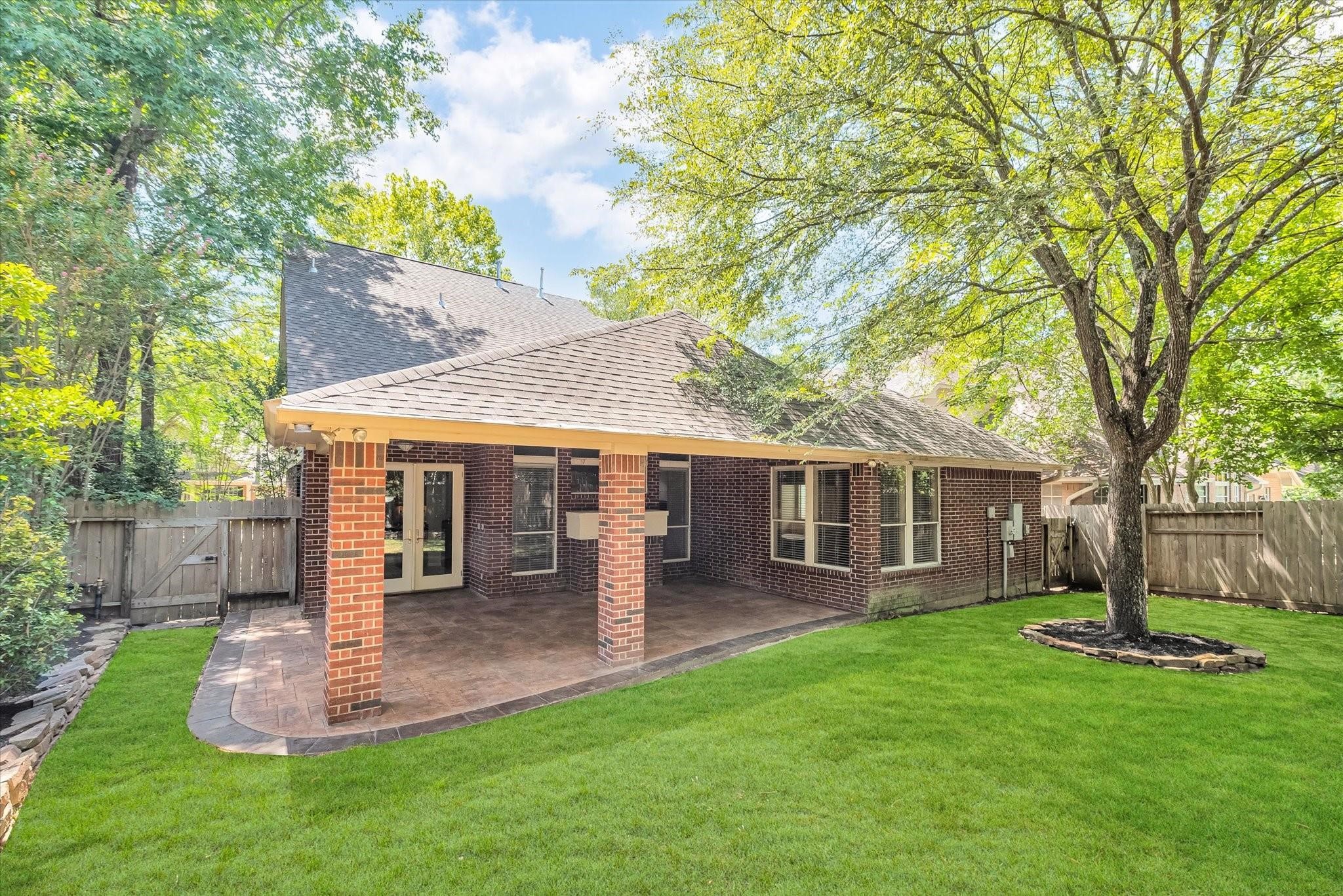 Back elevation of the home showing the beautiful trees and wooded aesthetics, lush lawn, and covered back patio.