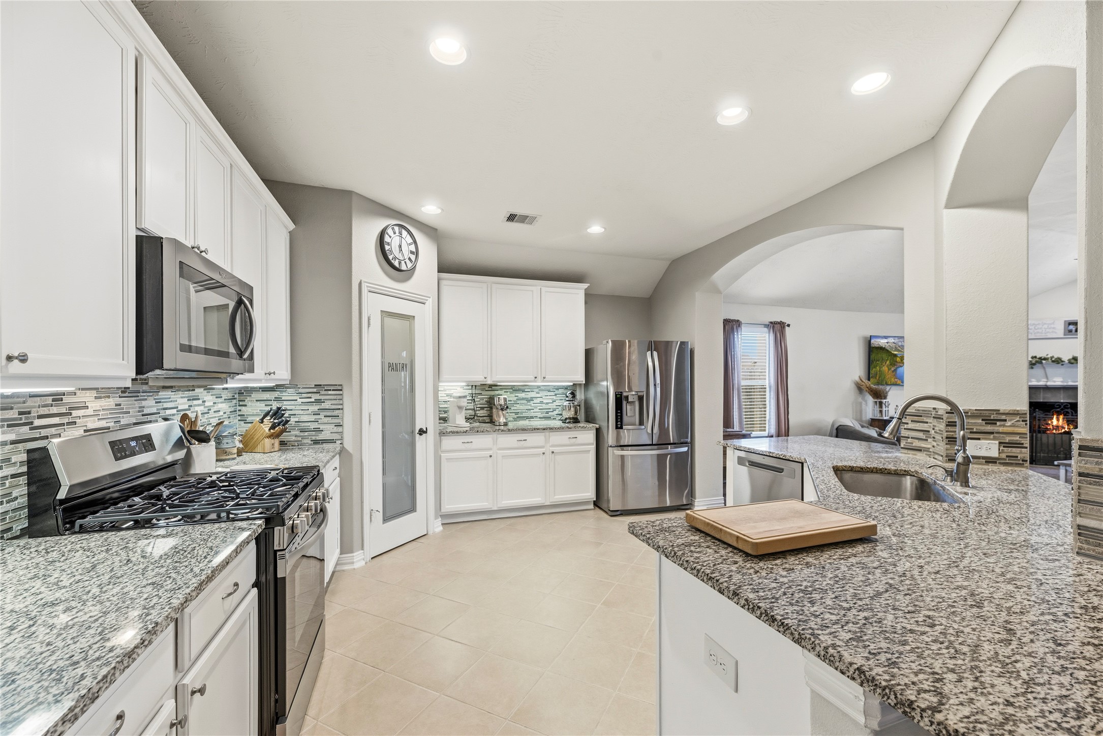 Gorgeous kitchen features granite countertops, glass tile backsplash, white cabinetry, under cabinet lighting, stainless steel appliances and a gas range.