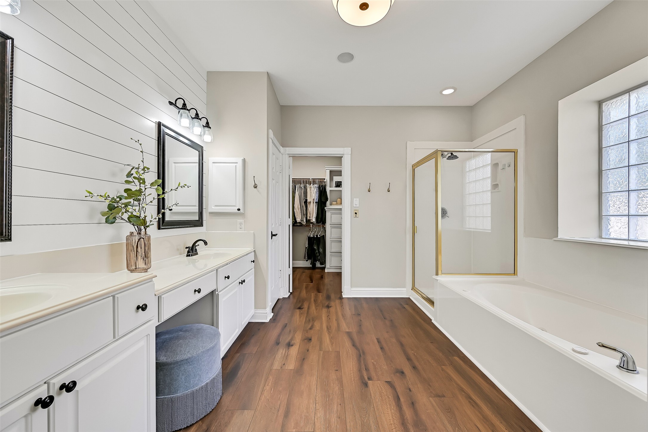 The spacious primary bath offers an extended dual-sink vanity with dedicated seated makeup space, abundant cabinetry & a shiplap accent wall. LVP flooring continues into the bath, with the oversized walk-in closet conveniently located just beyond.