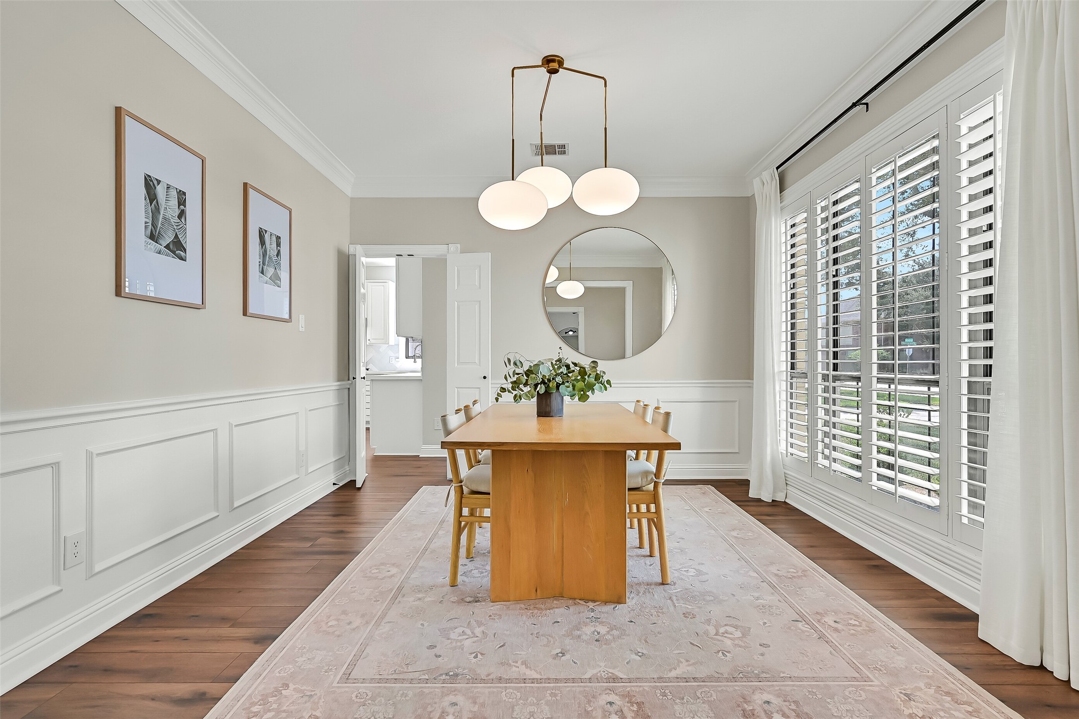 The elegant formal dining room features timeless plantation shutters, crown molding, chair rail & detailed picture-frame millwork. A large front-facing window fills the room with natural light, while LVP flooring provides a seamless transition from the foyer.