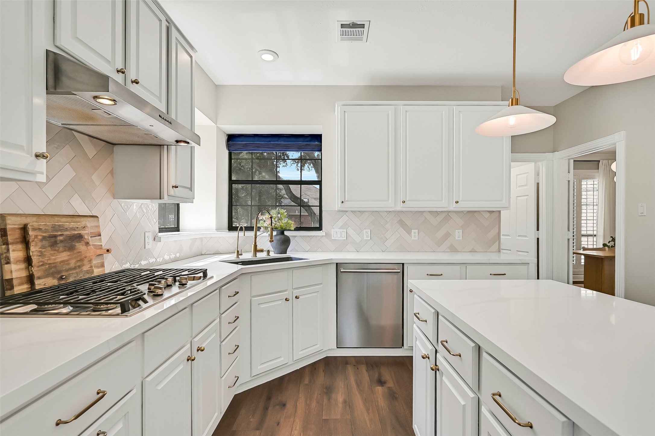 The spacious kitchen offers an abundance of cabinetry and workspace, including a large center island with seating. Quartzite counters, crisp white cabinetry, herringbone backsplash, gold-tone hardware & pendant lighting give the space a fresh, timeless look.